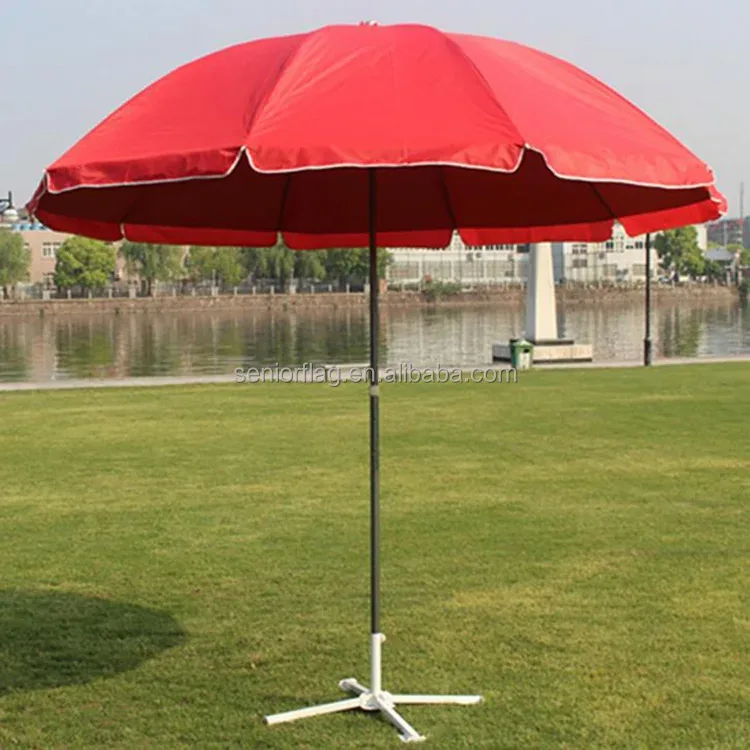 Red custom advertising parasol on a white metal cross stand in a park