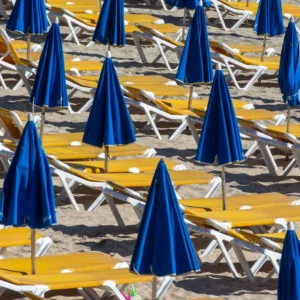 Closed blue beach umbrellas beside sun loungers