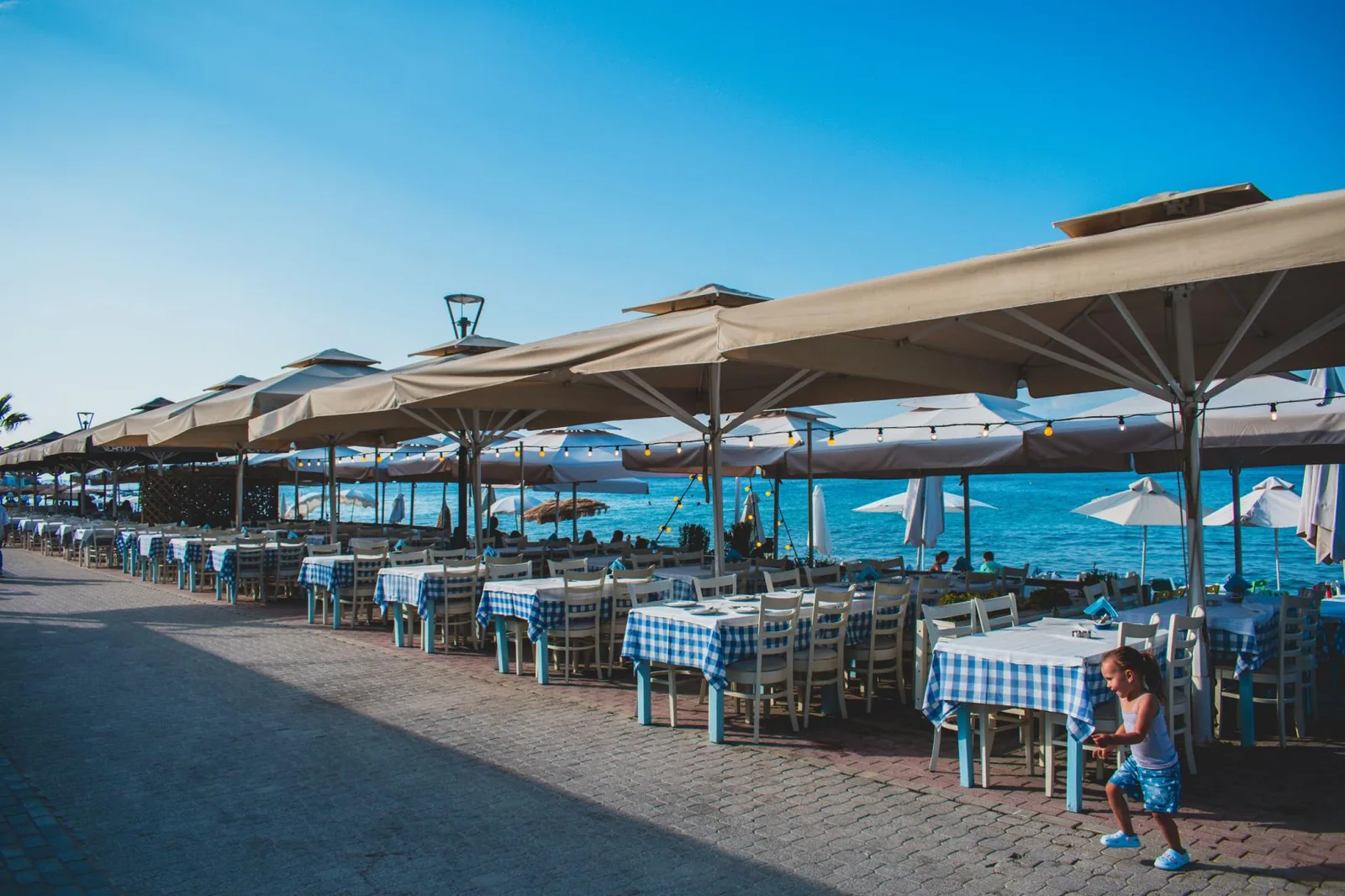 Beige patio umbrellas shading tables along a seaside promenade