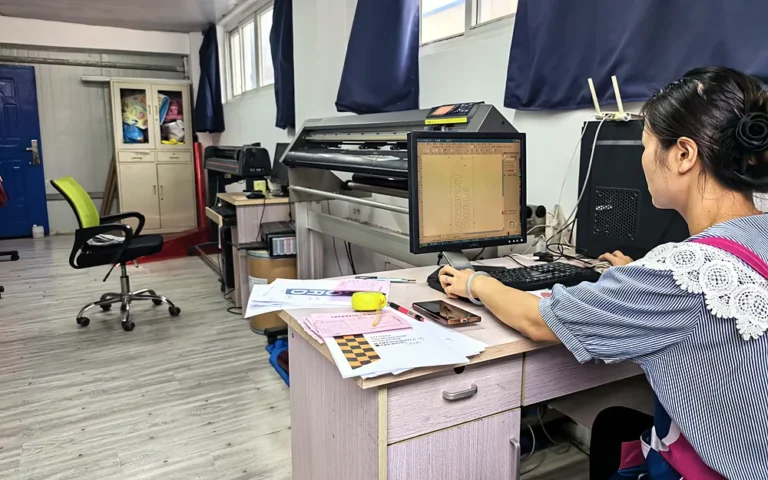 Staff preparing flag artwork and cutting files at a computer beside a cutting plotter