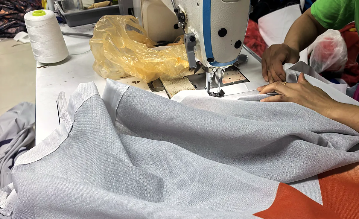 Close-up of a worker stitching the hem of a printed flag on an industrial sewing machine